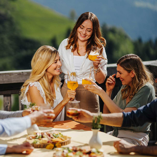 drei Freundinnen in einer Alpenlandschaft stoßen mit Gurktaler Sanddorn an